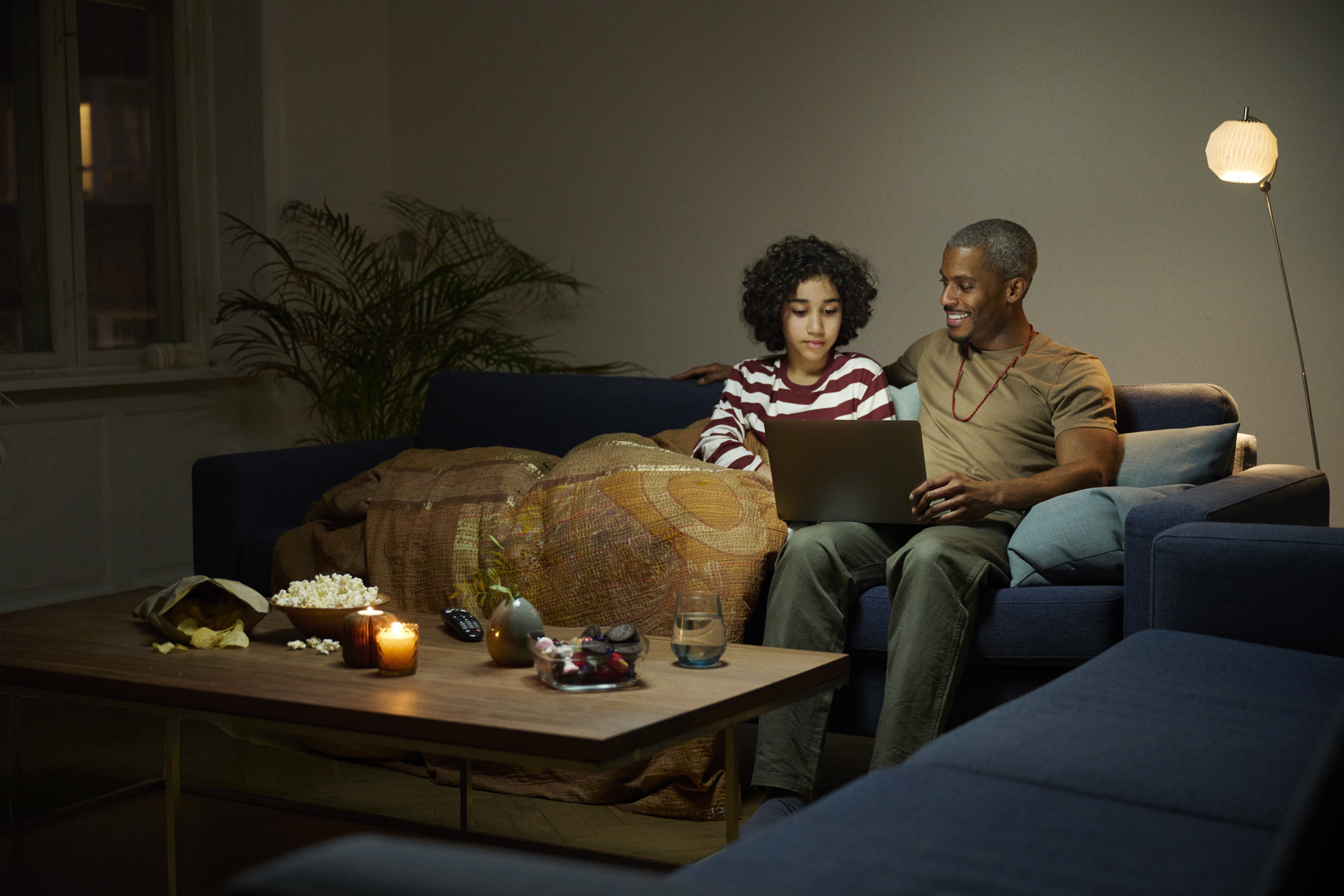 Man sitting in sofa with child, looking at a laptop together. 