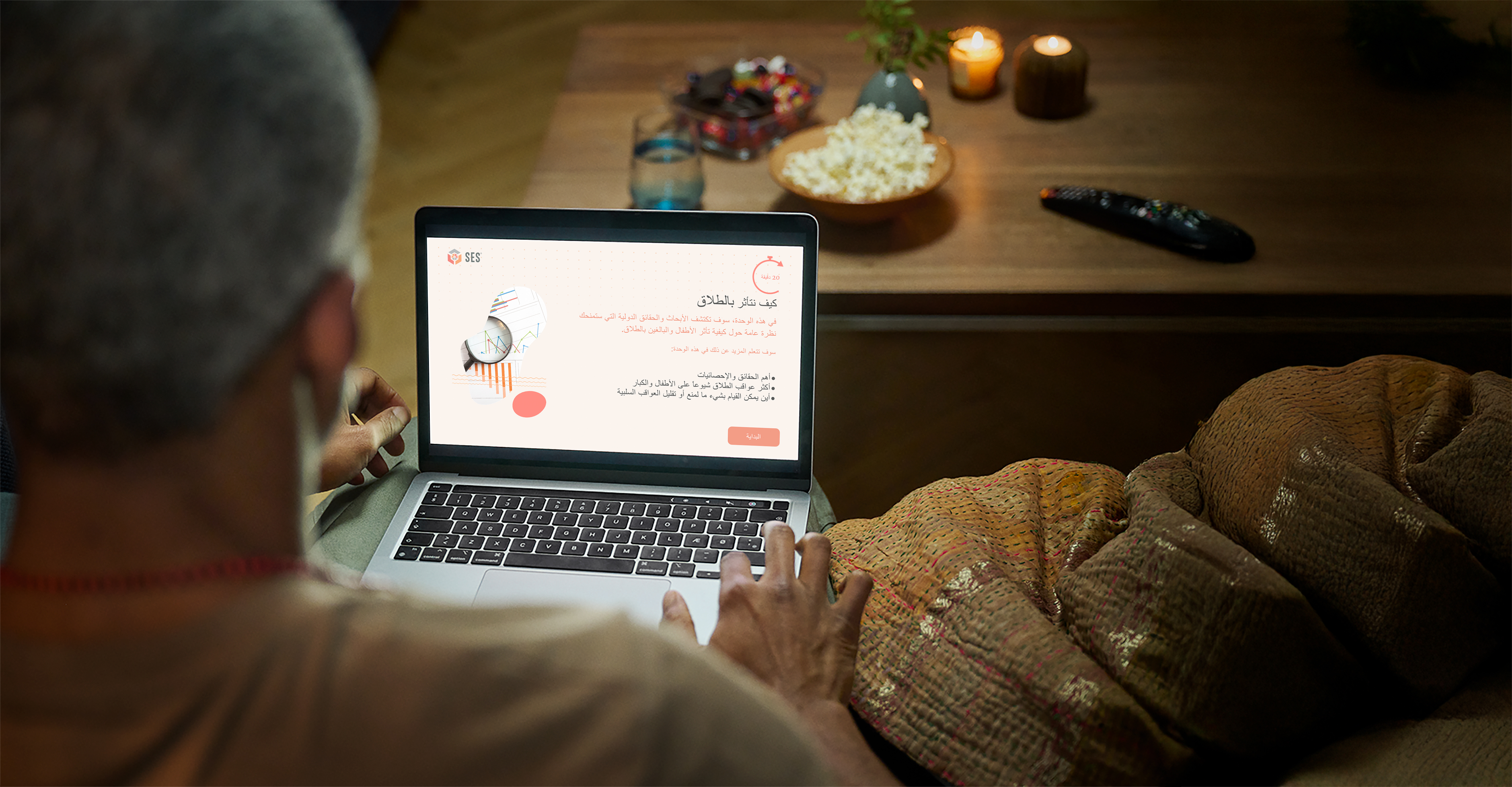 Over the shoulder view of a man sitting on a couch using the SES website with snacks on the table. 